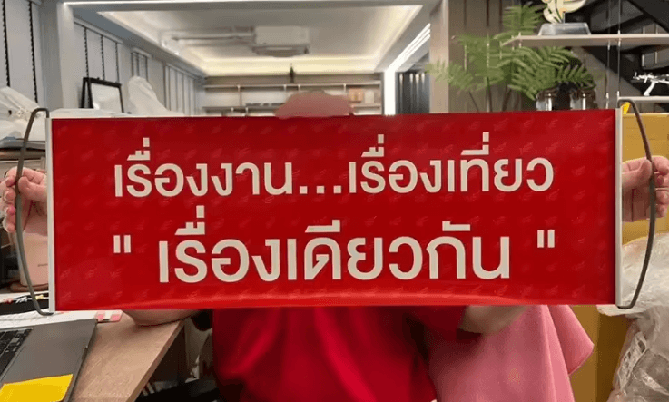 Red retractable handheld banner with Thai text 'เรื่องงาน...เรื่องเที่ยว เรื่องเดียวกัน' for event promotion