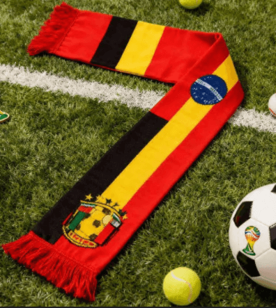 A red, black, and yellow striped custom made soccer scarf laid on artificial turf beside a football, showcasing soccer scarves custom designed for national team supporters.
